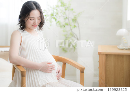 一位日本孕婦面帶微笑,一手放在肚子上,這是一張略帶憂傷的孕婦生活照。 一位日本孕婦面帶微笑,一手放在肚子上,這是一張略帶憂傷的孕婦生活照。 139928825
