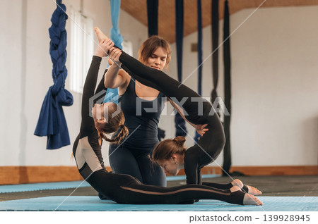 Three people are together. Female instructor helping a children practice yoga in a fitness studio Three people are together. Female instructor helping a children practice yoga in a fitness studio 139928945