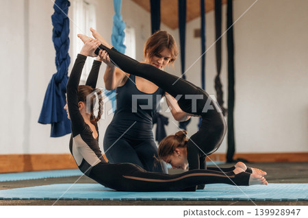 Three people are together. Female instructor helping a children practice yoga in a fitness studio Three people are together. Female instructor helping a children practice yoga in a fitness studio 139928947