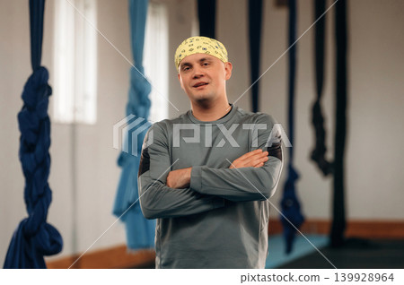 Male instructor is indoors with aerial yoga on hammock straps in a fitness studio Male instructor is indoors with aerial yoga on hammock straps in a fitness studio 139928964