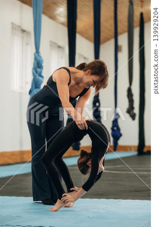 Female instructor helping a child practice yoga in a fitness studio Female instructor helping a child practice yoga in a fitness studio 139929204