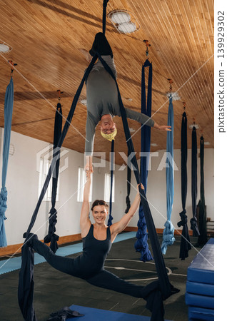 Teamwork conception. Male and female instructors practicing aerial yoga together in a fitness studio 139929302