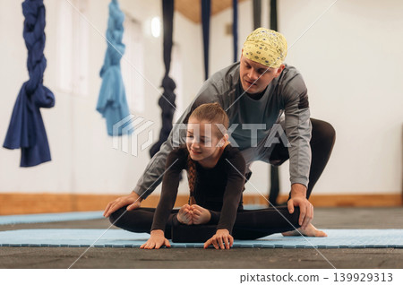 Male instructor assisting a child during yoga practice in a fitness studio Male instructor assisting a child during yoga practice in a fitness studio 139929313