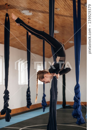 Hanging upside down. Child practicing aerial yoga on hammock straps in a fitness studio Hanging upside down. Child practicing aerial yoga on hammock straps in a fitness studio 139929379