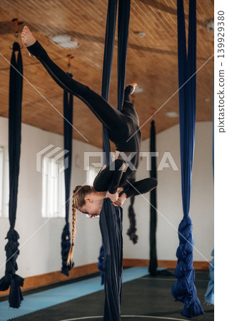Child practicing aerial yoga on hammock straps in a fitness studio 139929380