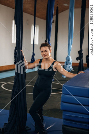 Pretty woman practicing aerial yoga on hammock straps in a fitness studio. Standing and smiling 139929561