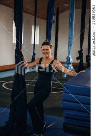 Pretty woman practicing aerial yoga on hammock straps in a fitness studio. Standing and smiling Pretty woman practicing aerial yoga on hammock straps in a fitness studio. Standing and smiling 139929562