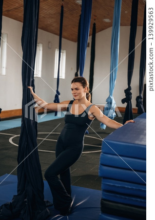 Pretty woman practicing aerial yoga on hammock straps in a fitness studio. Standing and smiling Pretty woman practicing aerial yoga on hammock straps in a fitness studio. Standing and smiling 139929563