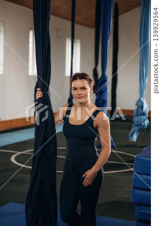 Pretty woman practicing aerial yoga on hammock straps in a fitness studio. Standing and smiling Pretty woman practicing aerial yoga on hammock straps in a fitness studio. Standing and smiling 139929564