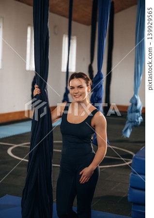 Pretty woman practicing aerial yoga on hammock straps in a fitness studio. Standing and smiling 139929565