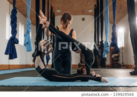 Difficult spine exercise. Female instructor helping a child practice yoga in a fitness studio Difficult spine exercise. Female instructor helping a child practice yoga in a fitness studio 139929568