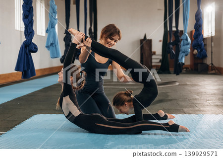 Busy by doing exercises. Female instructor helping a child practice yoga in a fitness studio Busy by doing exercises. Female instructor helping a child practice yoga in a fitness studio 139929571