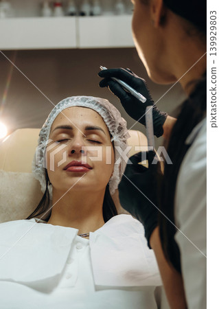 Marking the place. Female cosmetologist performing a facial skincare procedure using a cosmetic device in a beauty clinic Marking the place. Female cosmetologist performing a facial skincare procedure using a cosmetic device in a beauty clinic 139929803