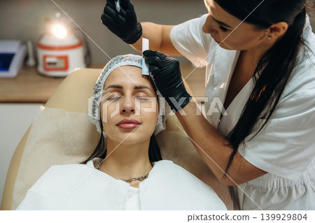 Marking the place. Female cosmetologist performing a facial skincare procedure using a cosmetic device in a beauty clinic 139929804