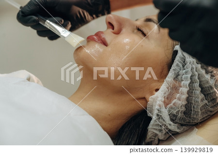 Brush, applying cream with it. Close-up of a facial skincare treatment with a cosmetic device in a beauty clinic Brush, applying cream with it. Close-up of a facial skincare treatment with a cosmetic device in a beauty clinic 139929819