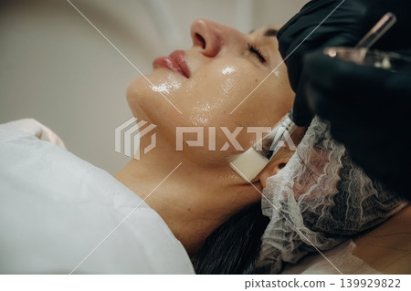 Rejuvenation process. Facial skincare treatment with a cosmetic device in a beauty clinic Rejuvenation process. Facial skincare treatment with a cosmetic device in a beauty clinic 139929822