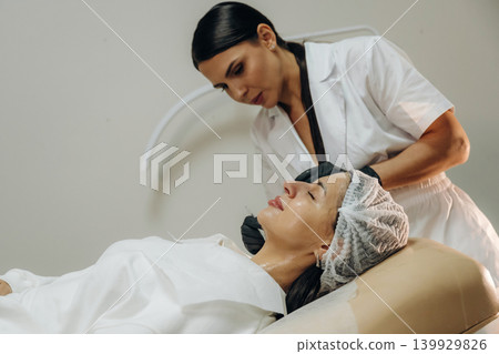 In black gloves. Female cosmetologist performing a facial skincare procedure using a cosmetic device in a beauty clinic 139929826