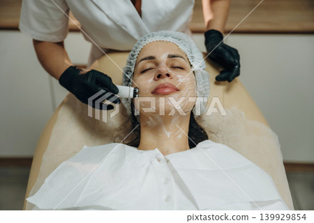 With eyes closed. Close-up of a facial skincare treatment with a cosmetic device in a beauty clinic With eyes closed. Close-up of a facial skincare treatment with a cosmetic device in a beauty clinic 139929854