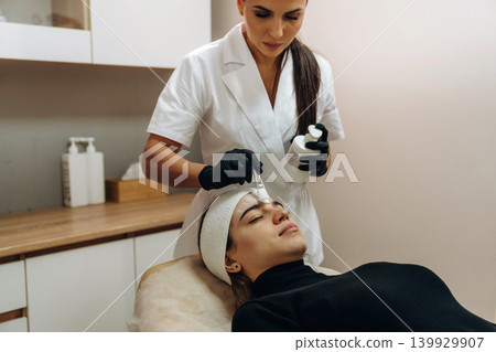 Female cosmetologist performing a facial skincare procedure using a cosmetic device in a beauty clinic Female cosmetologist performing a facial skincare procedure using a cosmetic device in a beauty clinic 139929907
