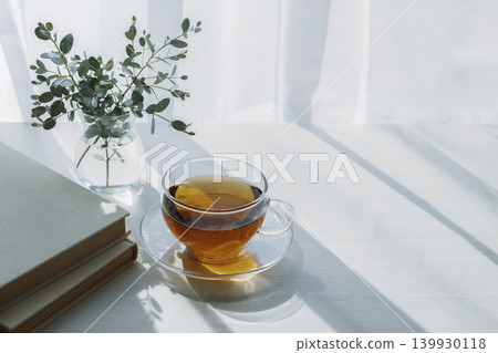 A quiet tea time with morning light, tea, and a book. 139930118