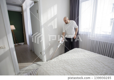 Young man using rechargeable wireless vacuum cleaner device at home. Young man using rechargeable wireless vacuum cleaner device at home. 139930285
