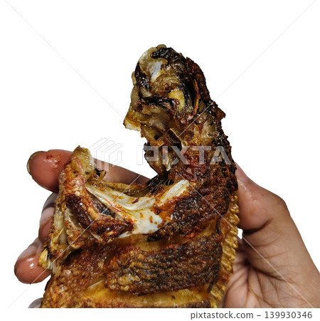 Detail of crispy fried fish head being held in hand. Detail of crispy fried fish head being held in hand. 139930346