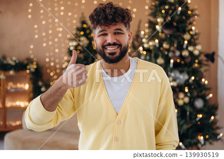 Man posing in front of a Christmas tree in a festive home setting Man posing in front of a Christmas tree in a festive home setting 139930519
