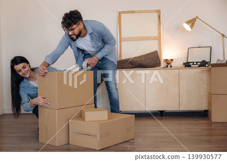 Using scotch as glue. Couple packing cardboard boxes while preparing to move into a new home Using scotch as glue. Couple packing cardboard boxes while preparing to move into a new home 139930577