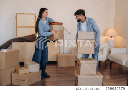 Walking and smiling. A couple carrying cardboard boxes while moving into a new apartment Walking and smiling. A couple carrying cardboard boxes while moving into a new apartment 139930579