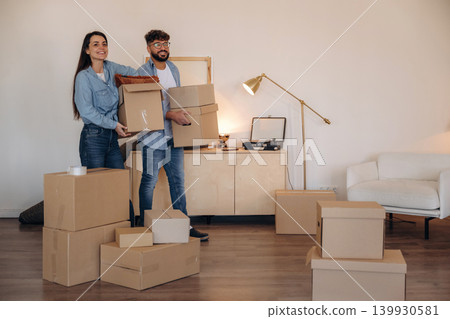 Walking and smiling. A couple carrying cardboard boxes while moving into a new apartment Walking and smiling. A couple carrying cardboard boxes while moving into a new apartment 139930581