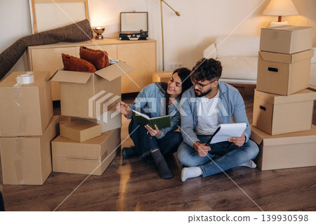 Sitting on the floor with notepads. Couple reviewing documents and planning their new home after moving Sitting on the floor with notepads. Couple reviewing documents and planning their new home after moving 139930598