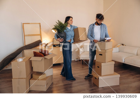 Woman is holding big green plant. Couple reviewing documents and planning their new home after moving Woman is holding big green plant. Couple reviewing documents and planning their new home after moving 139930609