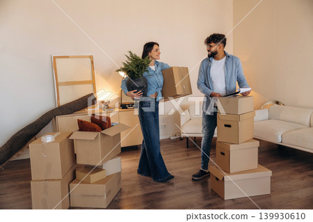 Woman is holding big green plant. Couple reviewing documents and planning their new home after moving Woman is holding big green plant. Couple reviewing documents and planning their new home after moving 139930610