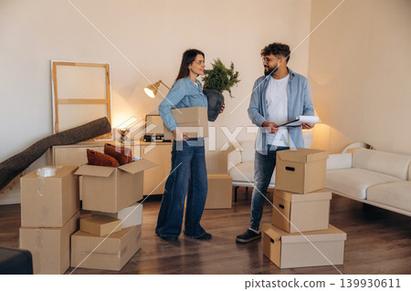 Woman is holding big green plant. Couple reviewing documents and planning their new home after moving Woman is holding big green plant. Couple reviewing documents and planning their new home after moving 139930611
