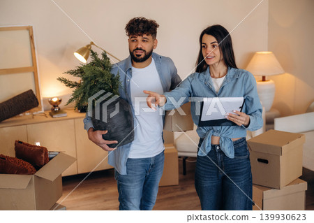 Man is with plant in hand. Couple reviewing documents and planning their new home after moving 139930623