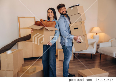 Standing together. A couple carrying cardboard boxes while moving into a new apartment Standing together. A couple carrying cardboard boxes while moving into a new apartment 139930647