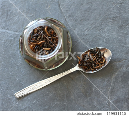 Edible mealworms , lat. Tenebrio molitor, in a spoon and bottle on the stone table. Edible mealworms , lat. Tenebrio molitor, in a spoon and bottle on the stone table. 139931110