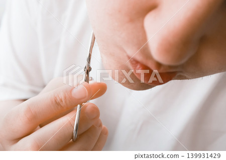 Close-up of a woman trimming unwanted chin hair with scissors during her home beauty routine. Managing facial hair removal due to hormonal changes. Close-up of a woman trimming unwanted chin hair with scissors during her home beauty routine. Managing facial hair removal due to hormonal changes. 139931429