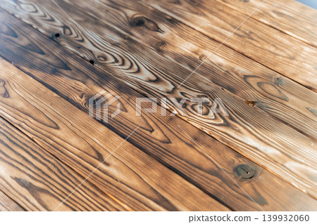 Close-up view of rustic wooden table surface showcasing natural grain patterns and textures with a warm brown finish and subtle highlights under soft lighting Close-up view of rustic wooden table surface showcasing natural grain patterns and textures with a warm brown finish and subtle highlights under soft lighting 139932060