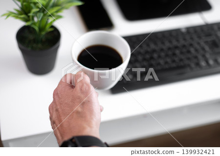 Hand Holding Cup of Black Coffee at Modern Home Office Desk Hand Holding Cup of Black Coffee at Modern Home Office Desk 139932421