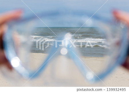 A view of the sea through blue diving goggles on the beach. Concept of a summer resort vacation and snorkeling. A view of the sea through blue diving goggles on the beach. Concept of a summer resort vacation and snorkeling. 139932495