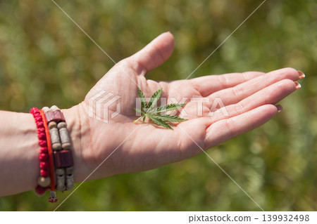 Female hand holding a green hemp leaf outdoors, close-up. Alternative medicine, CBD oil and natural cosmetics concept. 139932498