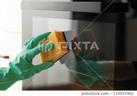 Cleaning the oven door with a sponge and a rubber glove, removing grease in a modern kitchen. Cleaning the oven door with a sponge and a rubber glove, removing grease in a modern kitchen. 139933462