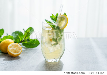 A summer drink with lemon, mint, and ice in a glass against a sunny window background. 139933464