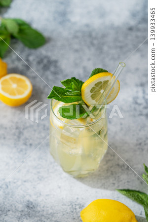 A summer drink with lemon, mint, and ice in a glass on a concrete background. A summer drink with lemon, mint, and ice in a glass on a concrete background. 139933465