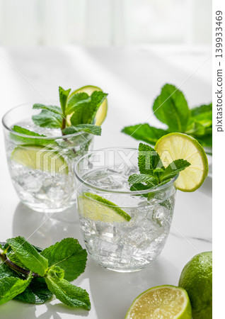 A fresh mojito with lime, mint and ice in glasses. Citrus lemonade or cocktail on a marble table A fresh mojito with lime, mint and ice in glasses. Citrus lemonade or cocktail on a marble table 139933469