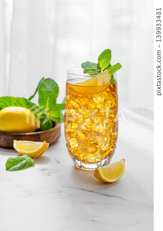 Iced tea with lemon and mint in a glass on a marble countertop with citrus fruits Iced tea with lemon and mint in a glass on a marble countertop with citrus fruits 139933481