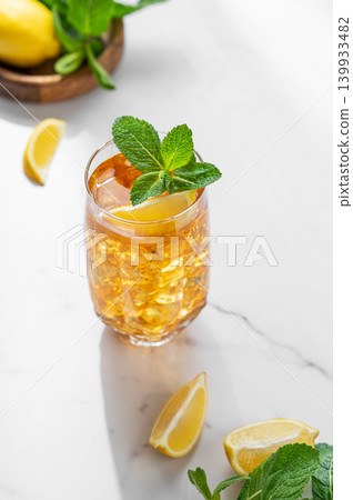 Iced tea with lemon and mint in a glass on a marble countertop with citrus fruits Iced tea with lemon and mint in a glass on a marble countertop with citrus fruits 139933482