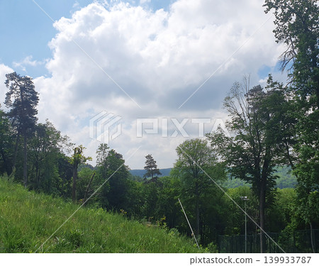 Scenic mountain landscape with green forested slopes under a bright blue summer sky with fluffy white clouds Scenic mountain landscape with green forested slopes under a bright blue summer sky with fluffy white clouds 139933787