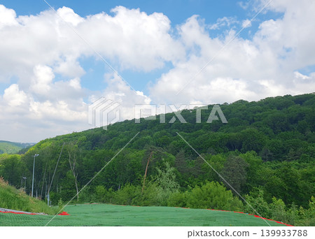 Scenic mountain landscape with green forested slopes under a bright blue summer sky with fluffy white clouds Scenic mountain landscape with green forested slopes under a bright blue summer sky with fluffy white clouds 139933788